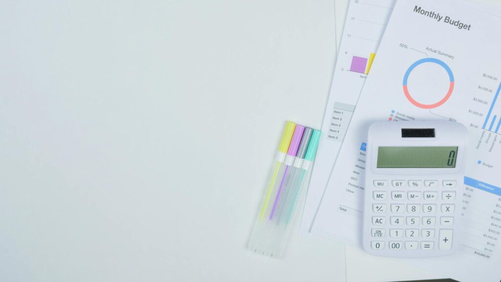 Minimalist office desk with a calculator, budget planning documents, and colorful pens.